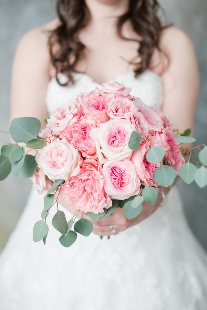 Bride holding out a bouquet of pink roses and peonies
