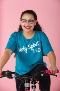 slime, purple, teal aqua, turquoise, pink, squishies, squishy's, bows, cheerleader, curly hair, orange, white bow, turquoise shirt, tween girl, 11 years old, fun, silly, holy spirit led t shirt pink backdrop, pink bicycle, glasses
