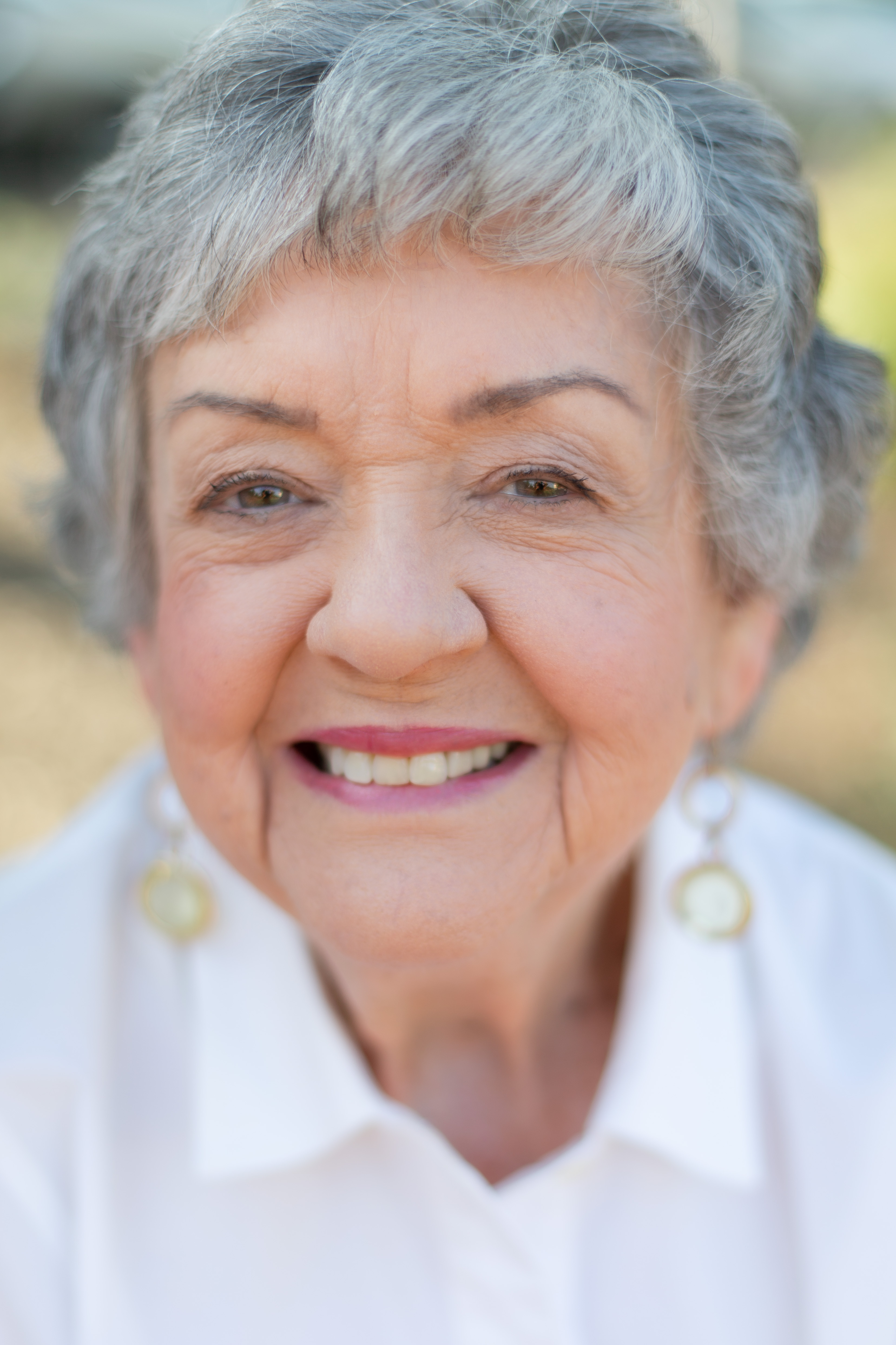 Grandmother smiles at camera with white shirt and gold earrings